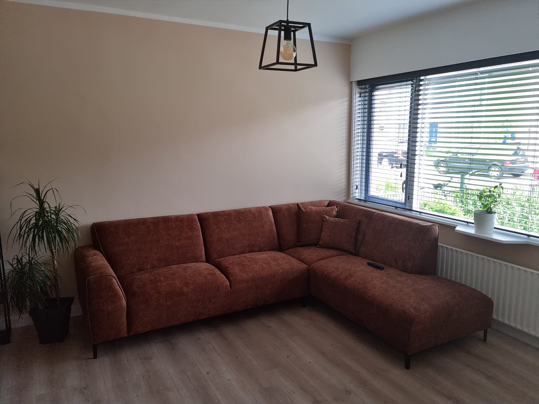 Woonkamer met vers geschilderde warme beige muren en een roestbruine hoekbank